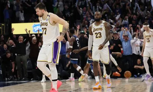 Luka Doncic (77) and LeBron James (23) of the Los Angeles Lakers walking on the basketball court during a game, with a crowd of cheering fans in the background.