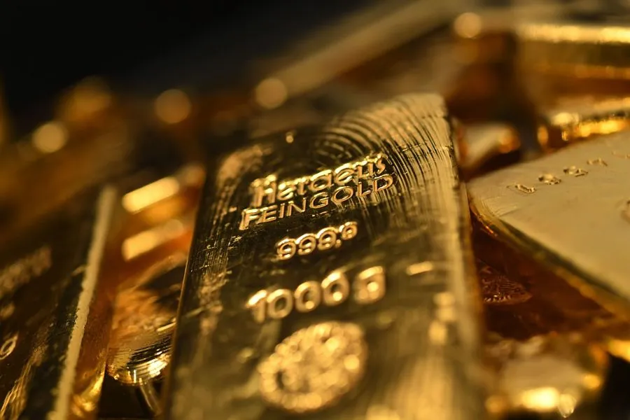A close-up, angled view of a shining gold bar stamped with "Heraeus FEINGOLD 999.9 1000g," surrounded by other blurred gold bars, emphasizing the tangible nature of precious metal investments.
