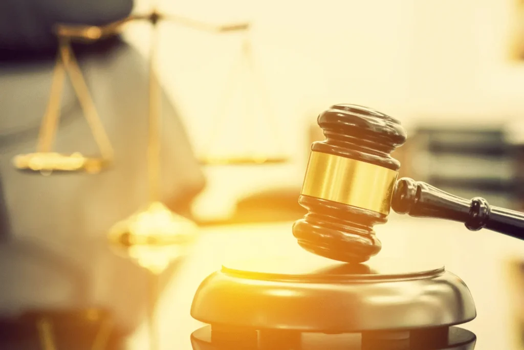 A warmly lit image featuring a judge's gavel on its block in the foreground, with the golden scales of justice visible in the soft-focus background, powerfully symbolizing legal proceedings and the pursuit of equity.