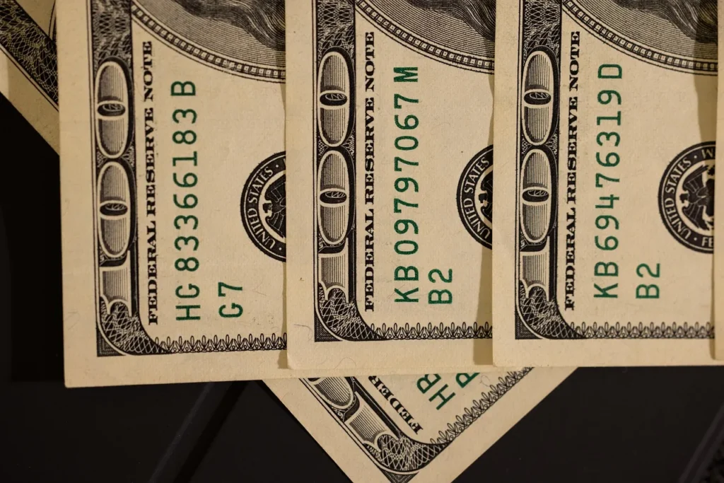 A close-up, high-angle view of several US hundred-dollar bills, fanned out to show the serial numbers and Federal Reserve markings, representing the financial transactions handled by merchant accounts.