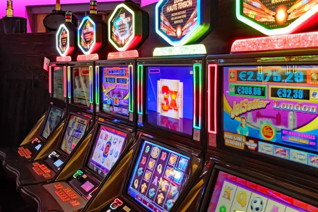 A row of brightly lit casino slot machines with various game displays.