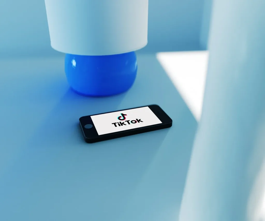 A 3D render of a smartphone lying on a bright blue surface, displaying the TikTok logo on its screen, symbolizing digital content and social media trends.